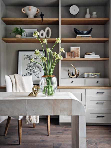 Close-up of home office with sculptural desk, fresh flowers in glass vase, built-in wood shelving with styled decor, and integrated drawers.