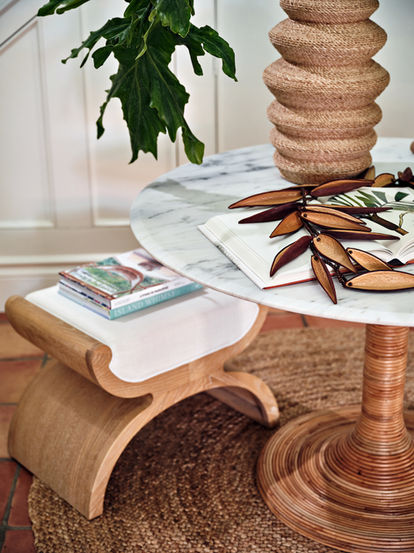 Close-up of entry table with stone tabletop, sculptural decor, curved wood stool, natural textures, and greenery.