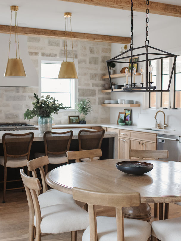Modern rustic kitchen with wood and stone elements, featuring a round dining table, barstools at a marble island, gold pendant lights, and a geometric chandelier.Palmer Kay Design_Interior Design_Peachtree City, GA