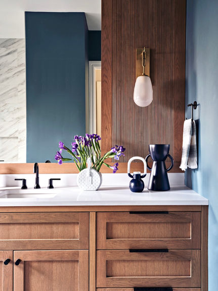 Bathroom with large mirror, white stone vanity countertop, dark blue walls, and wood cabinetry.