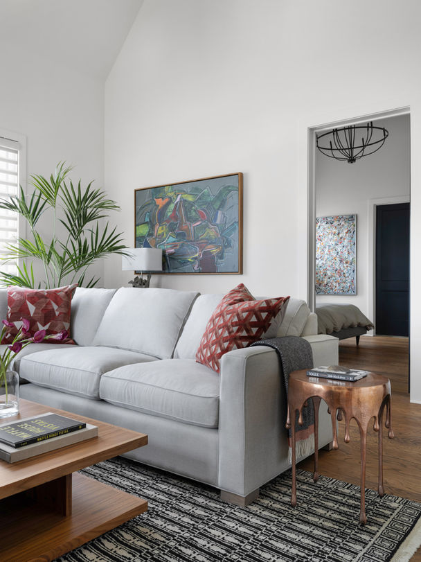 A modern living room with a gray sofa, red geometric pillows, abstract art, a potted plant, and a wooden coffee table. Palmer Kay Design_Interior Design_Peachtree City, GA