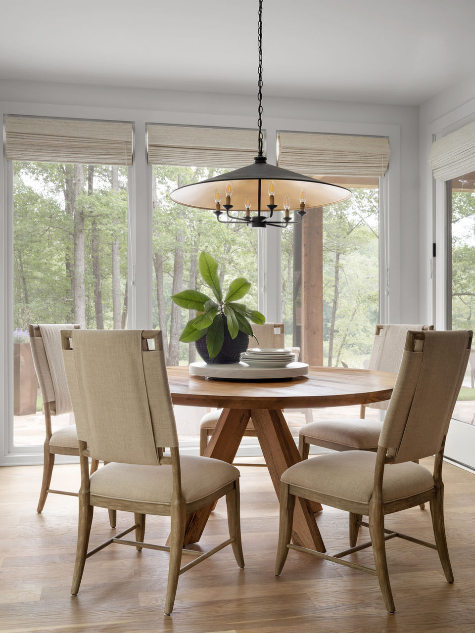 Dining area with a wooden table, four beige upholstered chairs, a black chandelier, and large windows overlooking a wooded area.
Palmer Kay Design_Interior Design_Peachtree City, GA