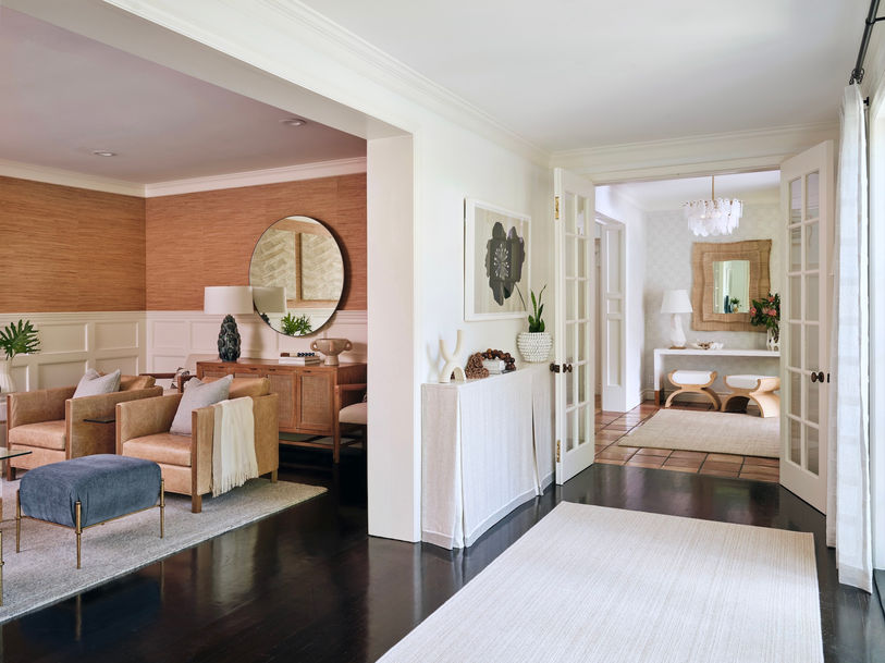 Interior view with entry hall, French doors, console table, adjacent living area with layered seating, textured walls, and round mirror.