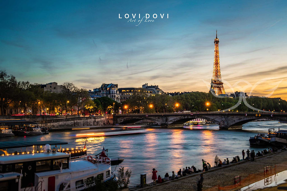 An enchanting view of the Eiffel Tower illuminated against the evening sky near Pont Alexandre III, with shimmering reflections dancing on the Seine and lively riverside activity. Photo by lovidovi.art