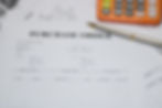 Purchase order form on a desk with a pen and an orange calculator. Background shows graphs and documents. Office setting, neutral mood.