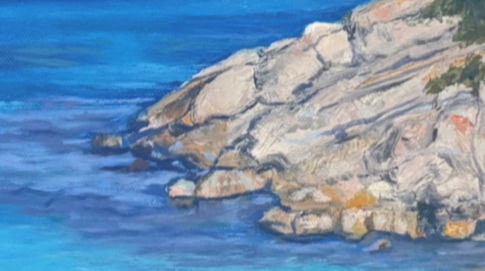 A close-up of a painted rocky shoreline meeting a serene blue sea, capturing the subtle textures and hues of the coastal landscape.