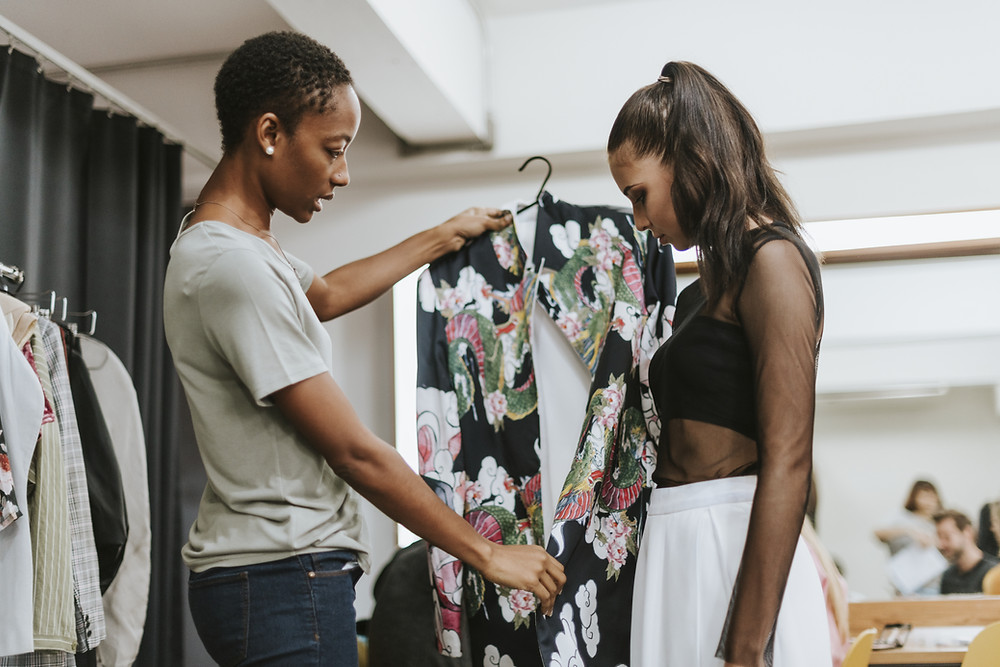 An african american stylist showing a dress to her female client.