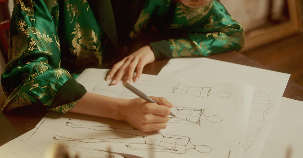 Designer's hands sketching designs using a fashion croquis.