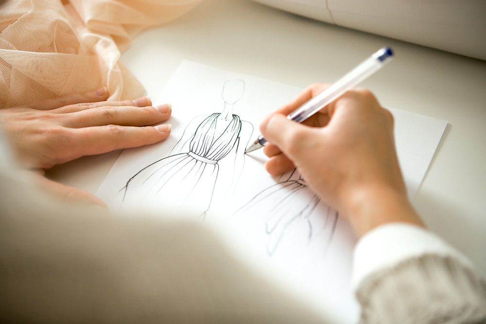 Caucasian female's hands holding a pen drawing a fashion sketch over a fashion croquis template.