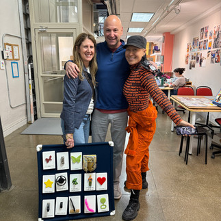 Three people smiling and posing, one holding a communication board.
