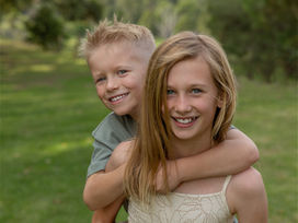 Smiling boy and girl piggyback, happy siblings outdoors