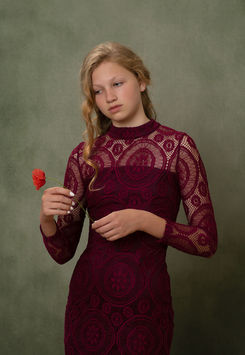 Young woman in burgundy lace dress holds single red flower