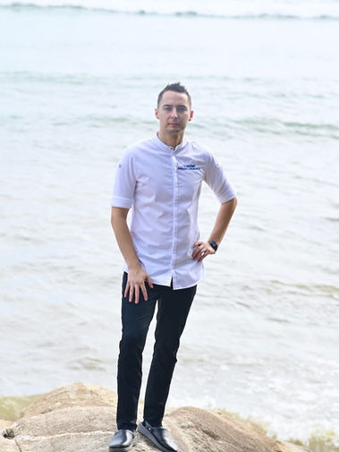 Executive Chef Maksym Chukonov standing alone on the beach in Phuket, gazing toward the sea, wearing a chef’s uniform — symbolizing inspiration, leadership, and connection to nature.