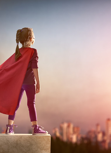 Little child girl plays superhero. Child on the background of sunset sky. Girl power conce