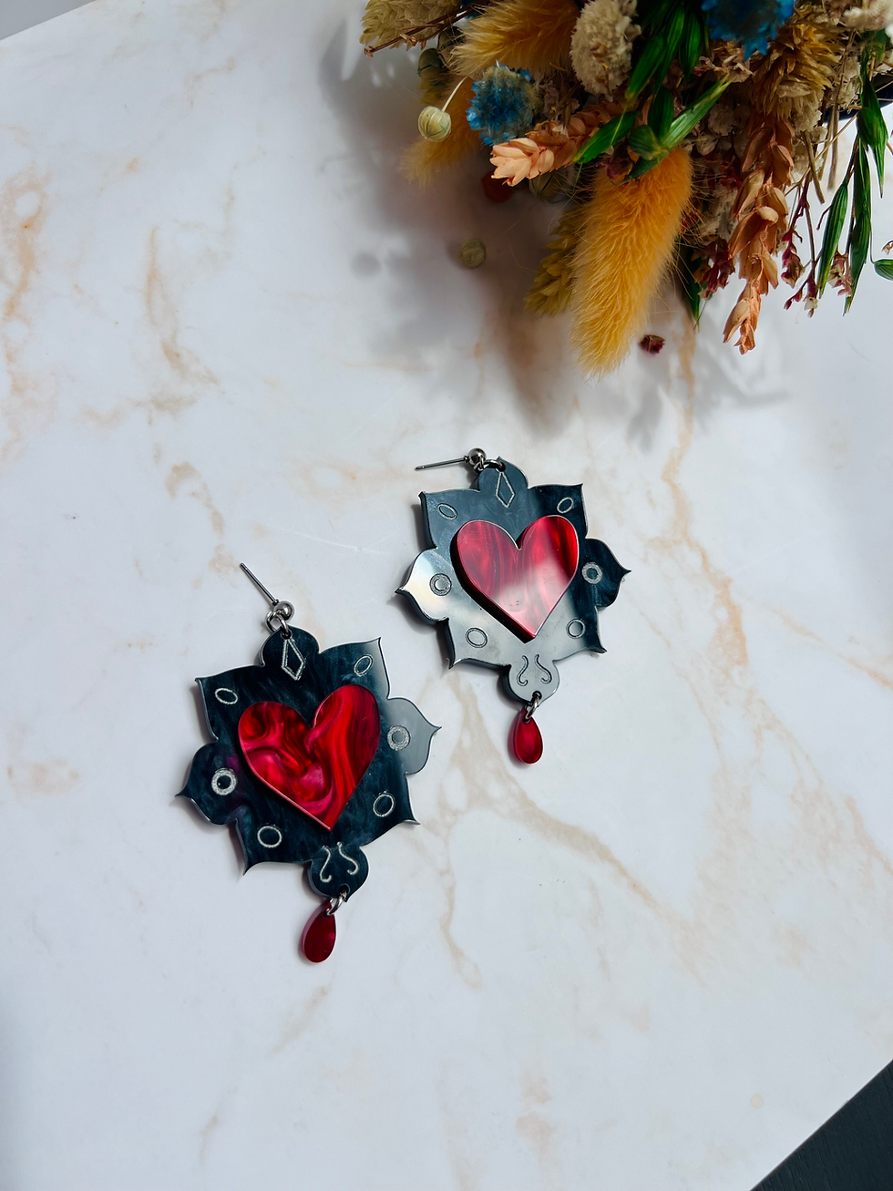 Miniatura: Pendientes negros con corazón rojo nacarados y detalles dorados sobre fondo de marmol