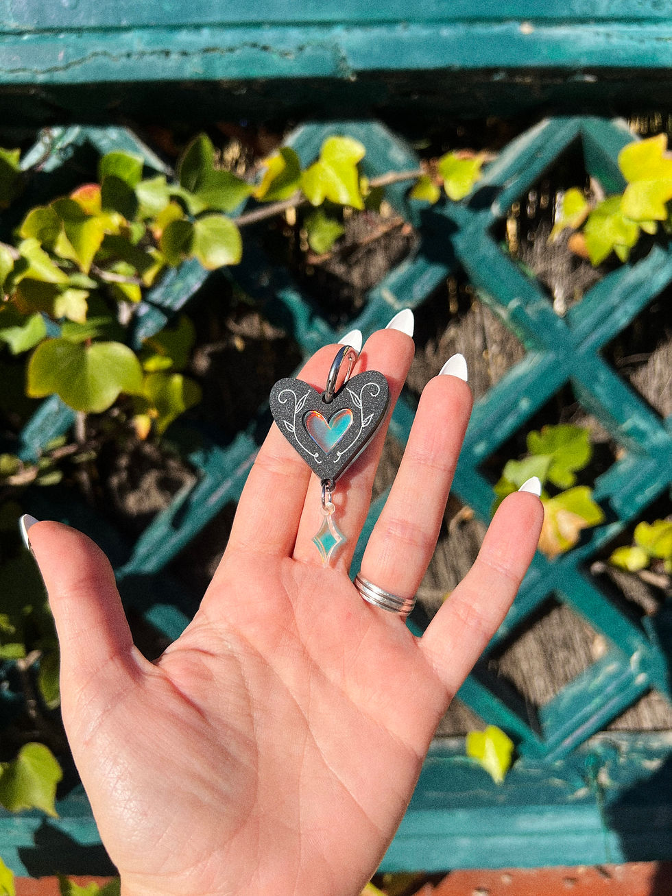 Miniatura: Mano sosteniendo Pendiente de corazón oscuro con corazón iridiscente en el centro y un rombo iridiscente golgando