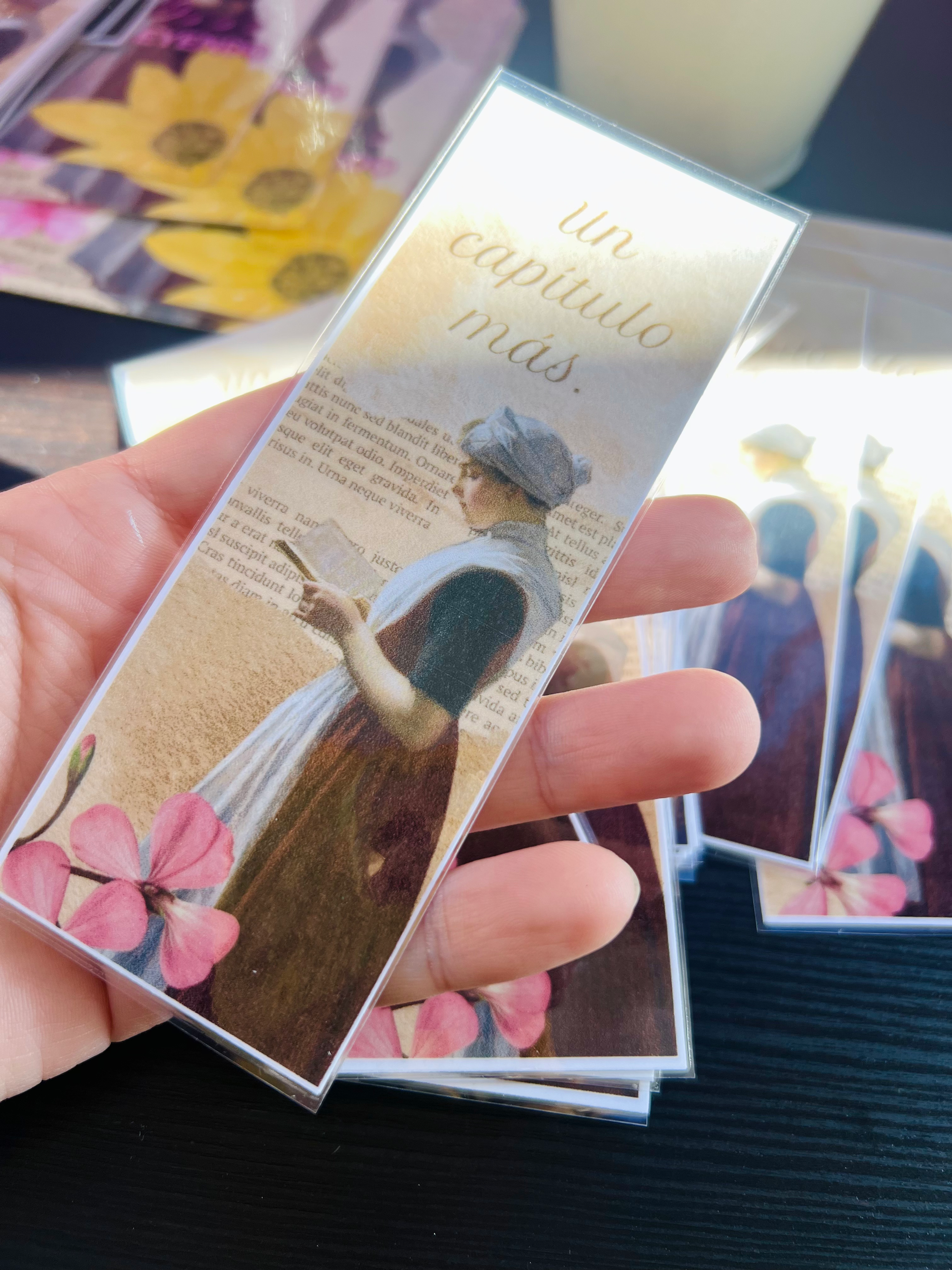 Marcador de libro con mujer, flores rosas y texto 'un capítulo más'.
