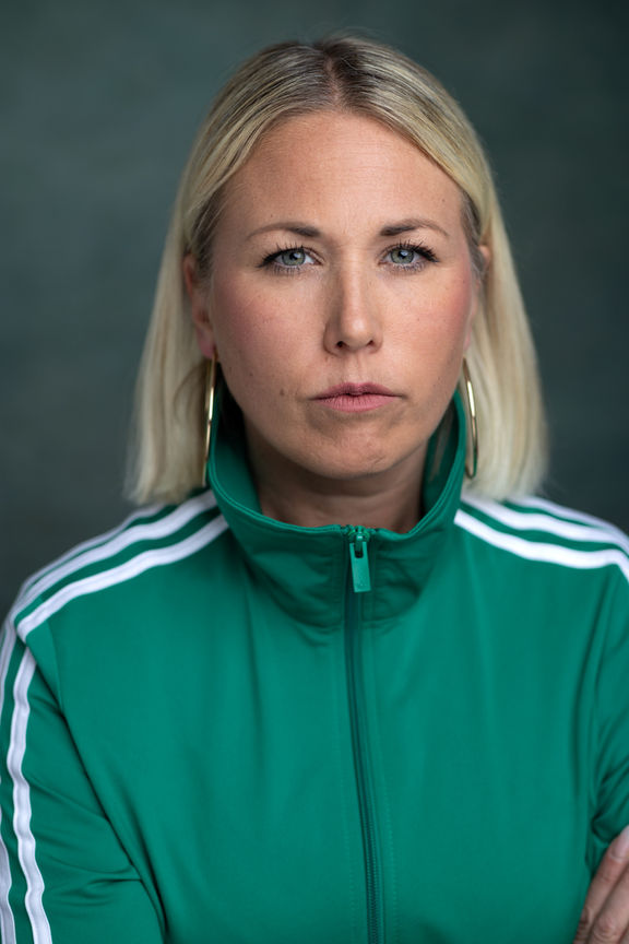 headshots - a female actor with blonde hair wearing a green tracksuit top sitting in front of a light green background