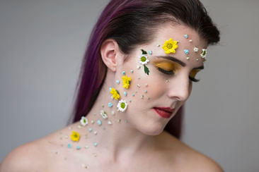 studio portrait of a woman with many dried flowers attached to the right hand side of her face