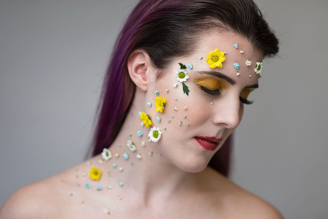 studio portrait of a woman with many dried flowers attached to the right hand side of her face
