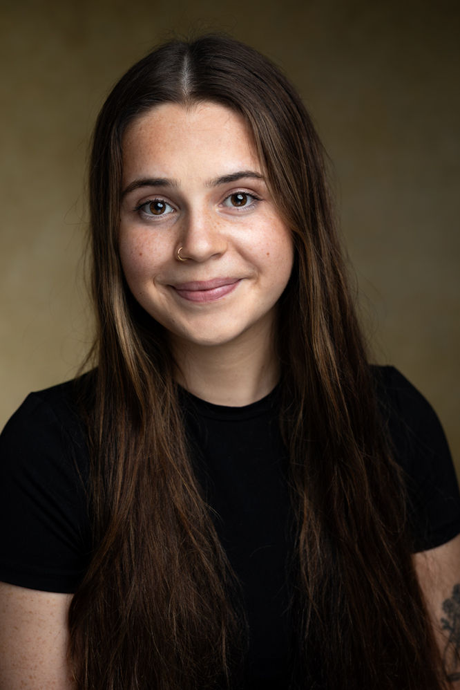 headshots - a female actor with brown hair wearing a black top in front of a beige background