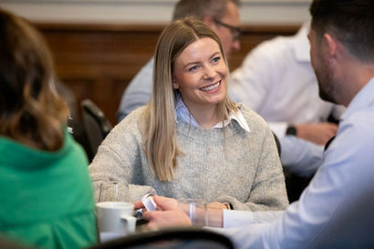 a seated woman smiles as she chats to a male colleague 