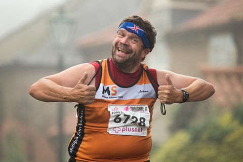 a male runner in the York Marathon smiles and gives a double 'thumbs up'.