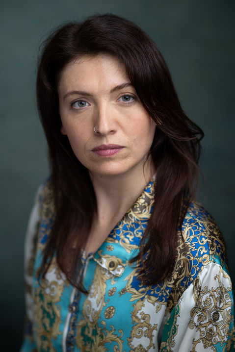 an actor with long dark brown hair wearing. Paisley shirt poses in front of a green backdrop