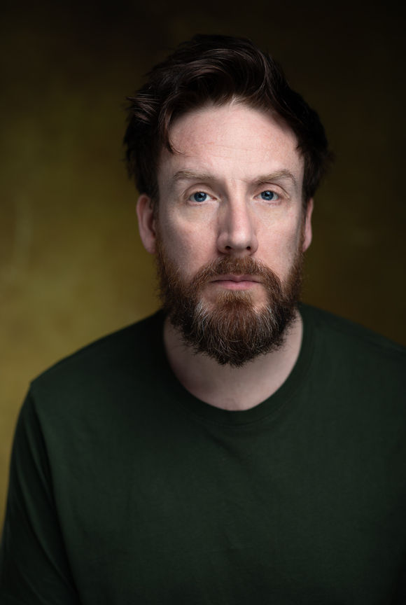 headshots - a male actor with a beard and wearing a dark green t-shirt poses against a green background