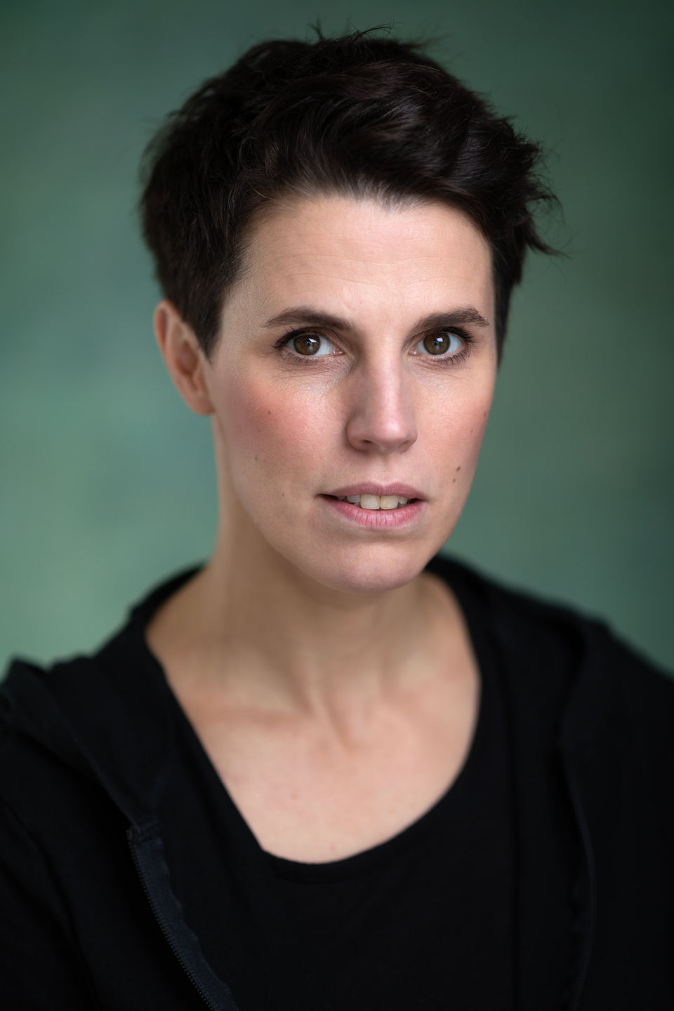 headshots - a female actor with black hair and wearing a black top sitting in front of a light green background