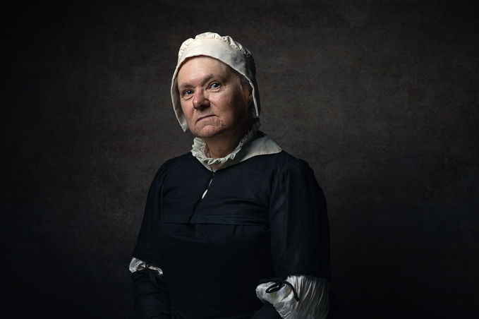 theatre - a female actor wearing contemporary costume stands in front of a dark brown background.