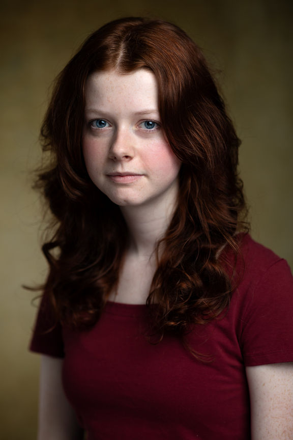 headshots - a young female actor with a deep red coloured jumper and red hair against a beige background