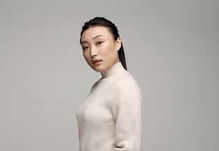 Sophie is an asian woman, wearing a white blouse. She has her hair up, and is standing in front of a beige wall.