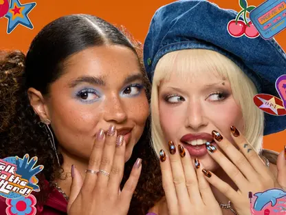 Divas jaunas sievietes ar 90. gadu stila iedvesmotu manikīru un grimu, fonā oranžs krāsojums un krāsaini uzlīmju motīvi ar frāzēm ‘Talk to the Hand!’, ‘As If!’ un citām retro ilustrācijām.