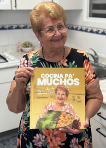 Abuela Enid poses with her book Cocina pa' muchos.