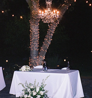 A candlelit table under a chandelier and twinkling lights for an intimate wedding moment.