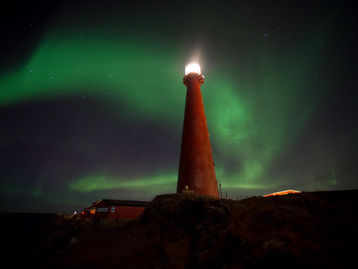 Northern Lights shining above Andøy Lighthouse on the coast of Northern Norway during an Arctic winter night.