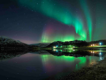 Northern Lights illuminating an Arctic beach in Northern Norway beneath a star-filled night sky.