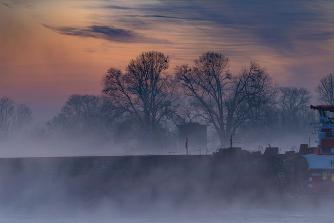 Das Bild zeigt einen malerischen Sonnenaufgang an einem Wintermorgen in Dormagen. Der Himmel ist in sanften Lila- und Rosatönen gefärbt, die eine friedliche und zauberhafte Atmosphäre schaffen. Der Nebel schwebt sanft über dem Rhein und verleiht der Szenerie eine mystische Note, während die Silhouetten der Uferlandschaft im Dunst verschwommen erscheinen.
Wandbild kaufen.