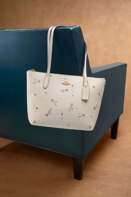 White Fiona Zip Tote with star print hanging from a deep teal chair against a warm brown background.