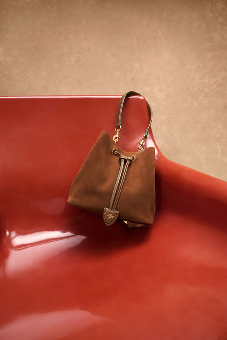 Vintage Brown Maple suede Faye Drawstring bag with quilting displayed on a glossy red chair.