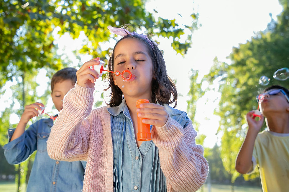 Children joyfully blowing bubbles and playing together outdoors, illustrating the joy and learning that come from play-based activities.