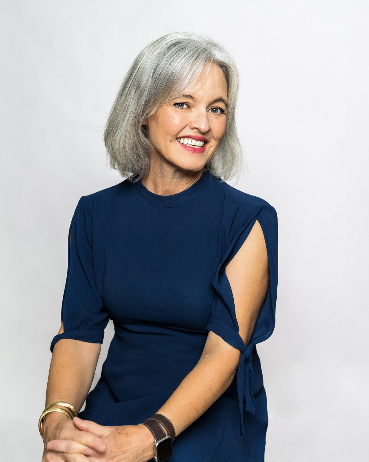 Professional portrait of a silver-haired woman in a teal dress with a confident smile, by Tina Dwyer Photography