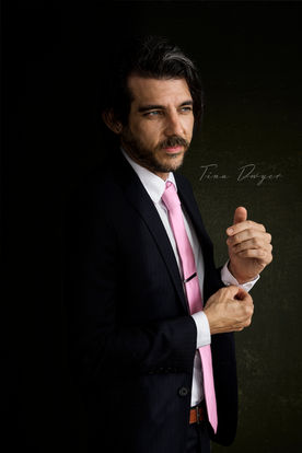 Dramatic studio portrait of a man in a black suit and pink tie with a strong, confident expression, by Tina Dwyer Photography