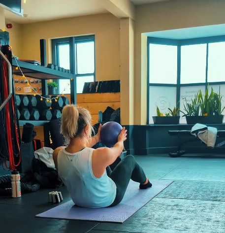 A lady doing Pilates on a mat with a ball