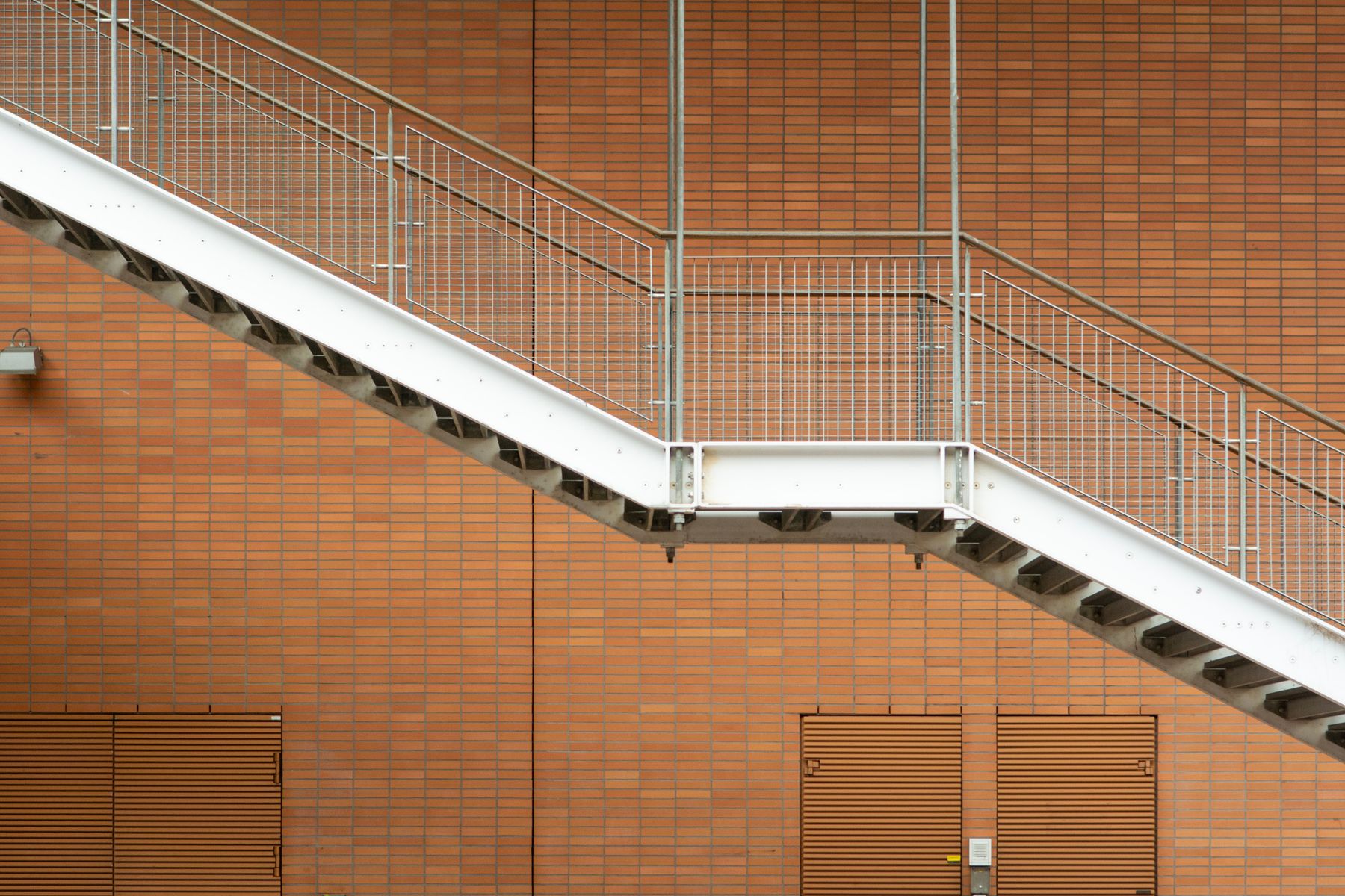 Side view of structural steel stairs showing steel stringers, landing, treads and metal handrails against a brick facade