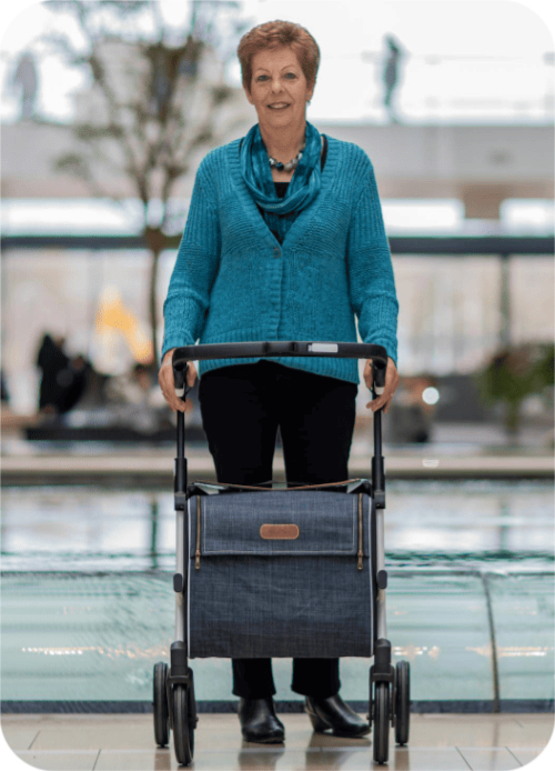 An older woman in a greenish-blue sweater, standing with a walker