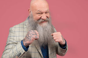 Photo book d'un homme chauve à la longue barbe en costume a carreaux qui tient ses ses main fermées et tatouée en position de boxe sur fond rose coloré pour une agence de  publicité par Guillaume Marbeck Photographe à Paris 8