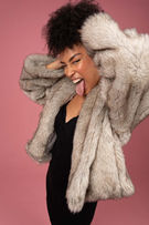 Photobook professionnel à paris pour mannequin Femme brune en fourrure sur fond rose grand sourire extraverti pour la publicité en tenue noire se tient les cheveux avec les mains pour on book photo de modèle