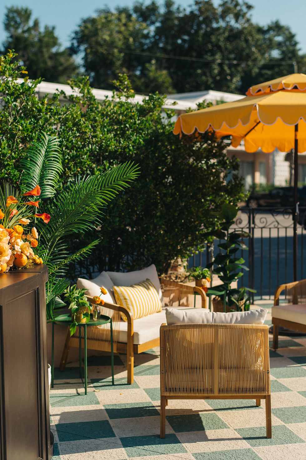 Outdoor pool patio with wicker chairs, green plants, and a yellow-striped pillow on a tiled floor. A bright yellow umbrella provides shade. Event Rentals for private events in North Charleston, SC